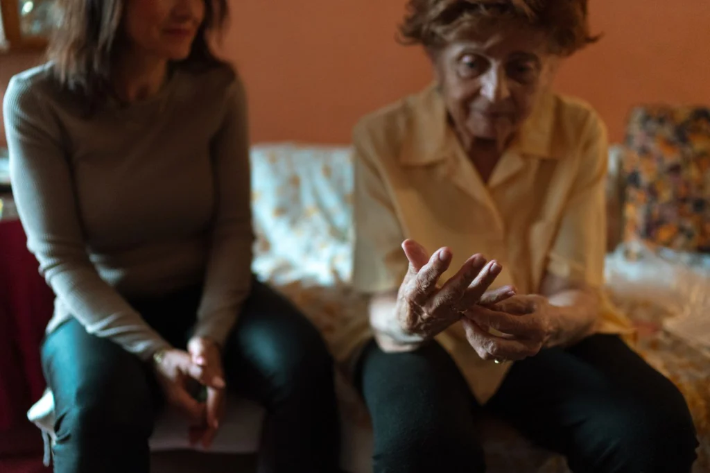A caregiver and an older woman talking together on a sofa at home